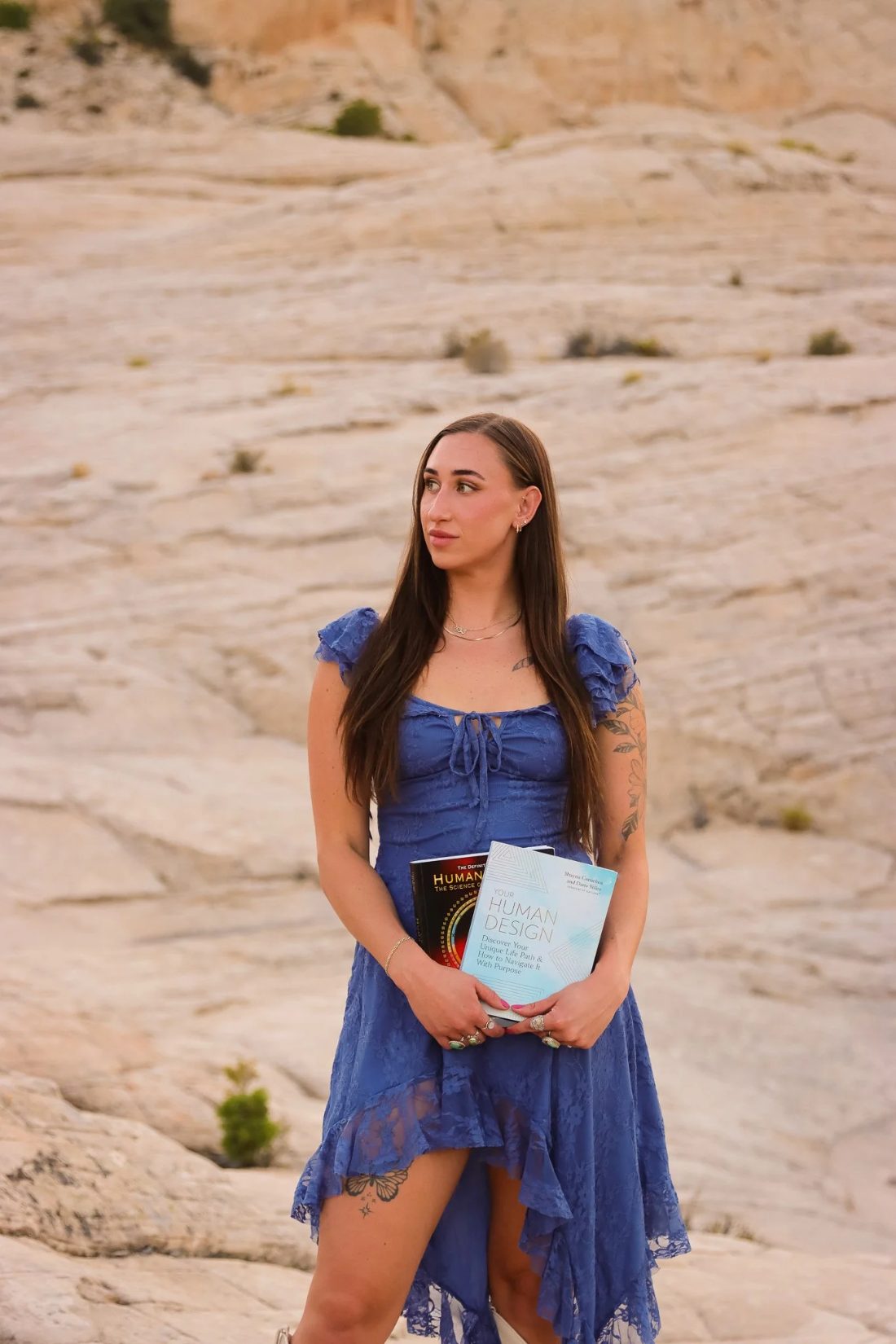 Cheyenne in a blue dress holding her Human Design books on the desert slickrock of St. George, Utah